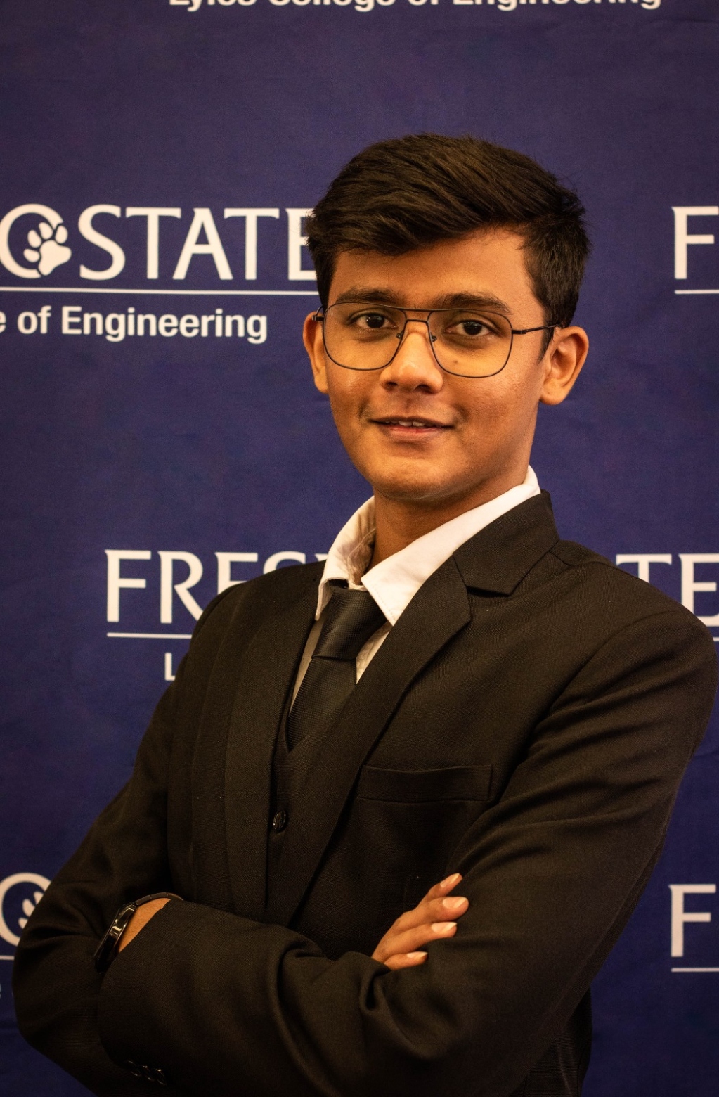 Ninad posing in black suit in front of Fresno State backdrop
