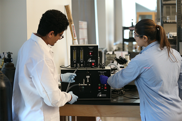 Students in lab coats working on a machine